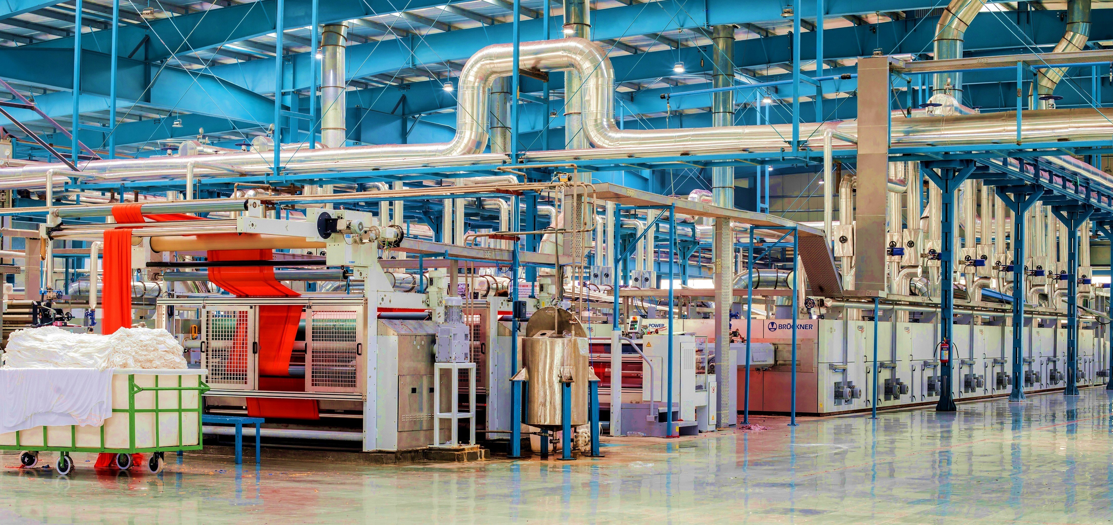 Industrial textile dyeing facility with Brückner machinery and bright orange fabric running through the production line